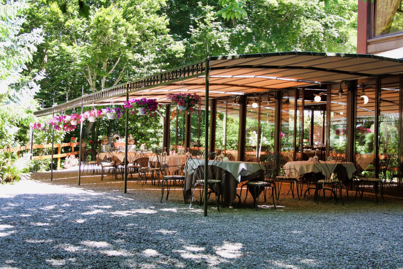 Ristorante all'aperto con tavoli apparecchiati e fiori appesi.