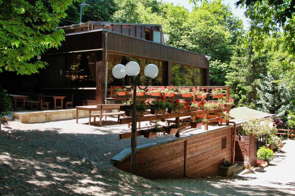Edificio in legno con terrazza fiorita, circondato da alberi.