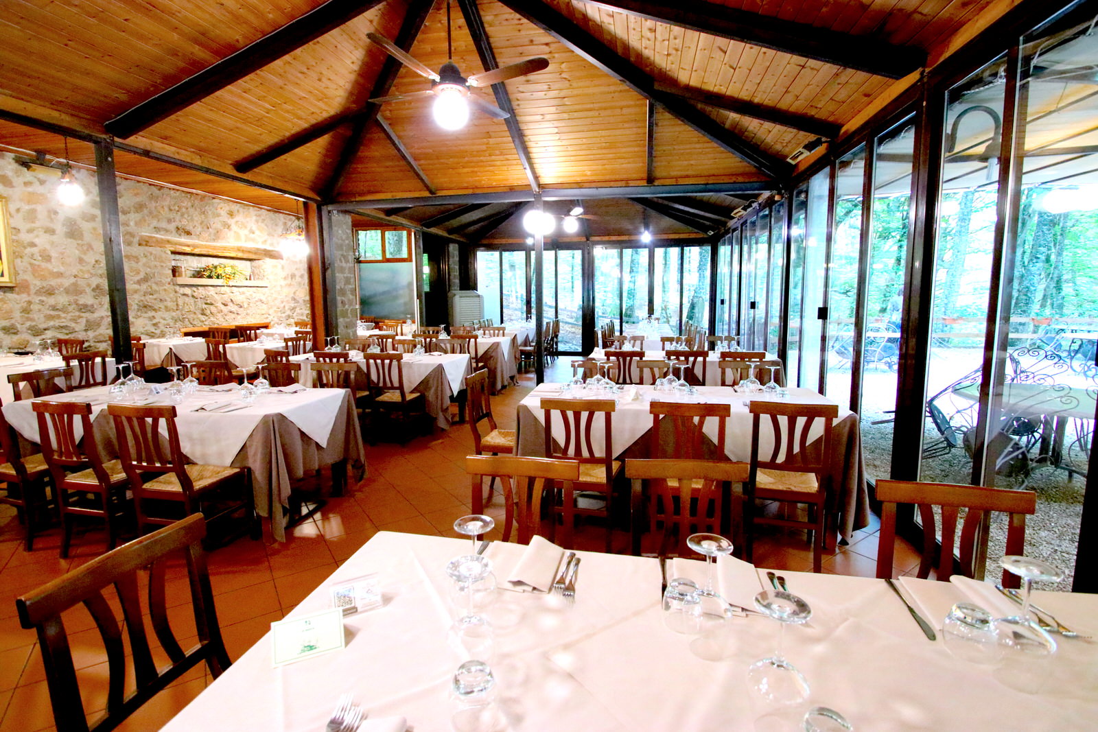 Ristorante con tavoli apparecchiati, soffitto in legno, pareti vetrate.