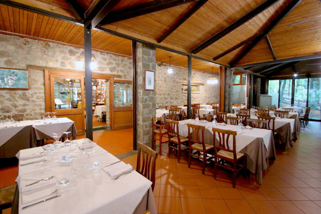 Ristorante con tavoli apparecchiati, interni in legno e pietra.