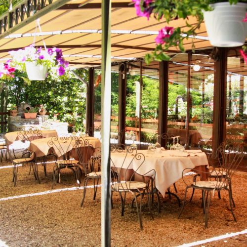 Terrazza di ristorante con tavoli apparecchiati e fiori appesi.