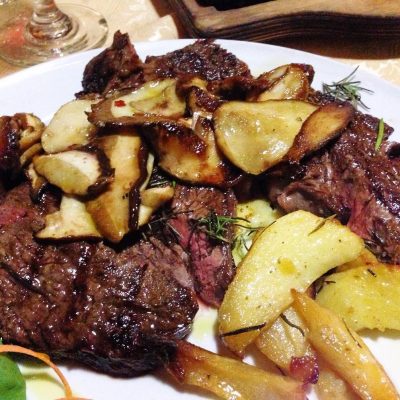 Bistecca con funghi e patate arrosto su piatto bianco.
