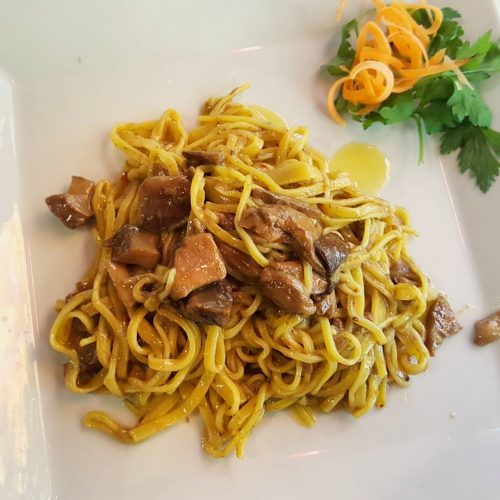 Tagliatelle ai funghi su piatto bianco, decorazione vegetale.