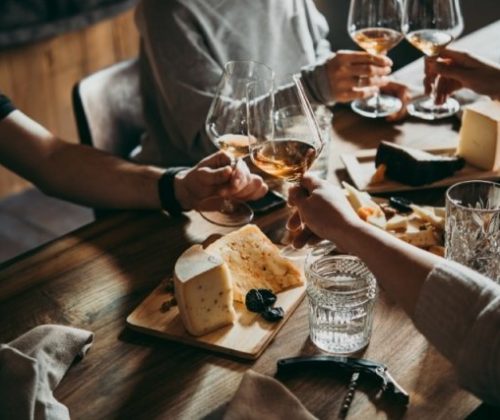Persone brindano con vino e formaggio su tavolo.