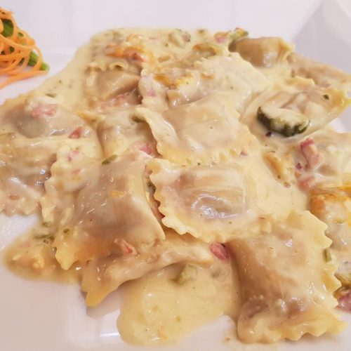 Ravioli con salsa cremosa su piatto bianco.