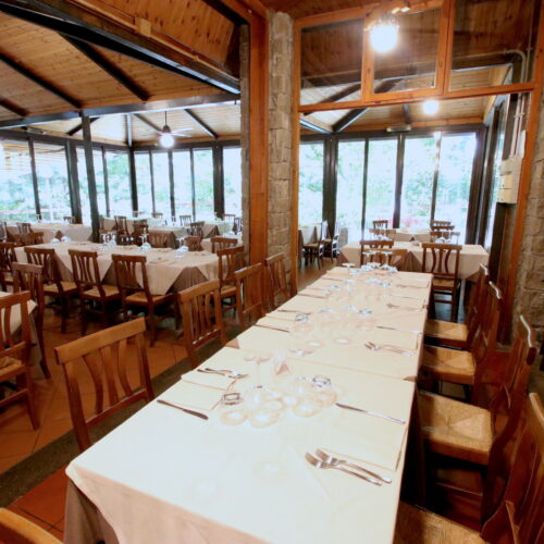 Sala da pranzo con tavoli apparecchiati e sedie in legno.