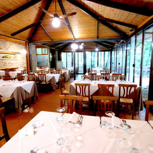 Ristorante con tavoli apparecchiati, soffitto in legno, pareti vetrate.