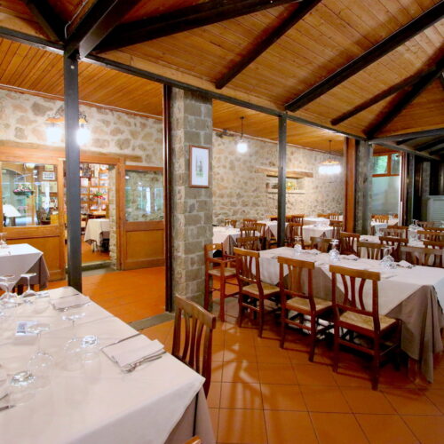 Ristorante rustico con tavoli apparecchiati e pareti in pietra.