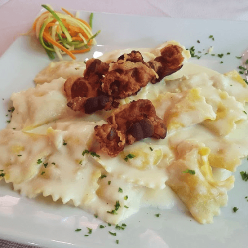 Ravioli con salsa bianca e guarnizione croccante su piatto.